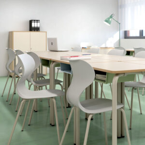 Sillas monobloc Mia Basic de silueta curva junto a pupitres square con bandeja inferior.